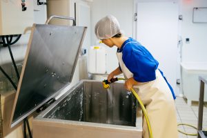 Factory worker washing tank for fermenting cheese